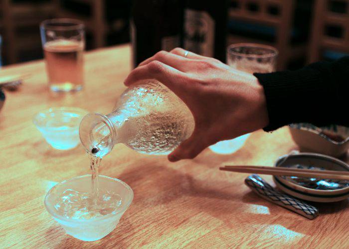 Someone holding a clear sake bottle and pouring sake into a glass sake cup.